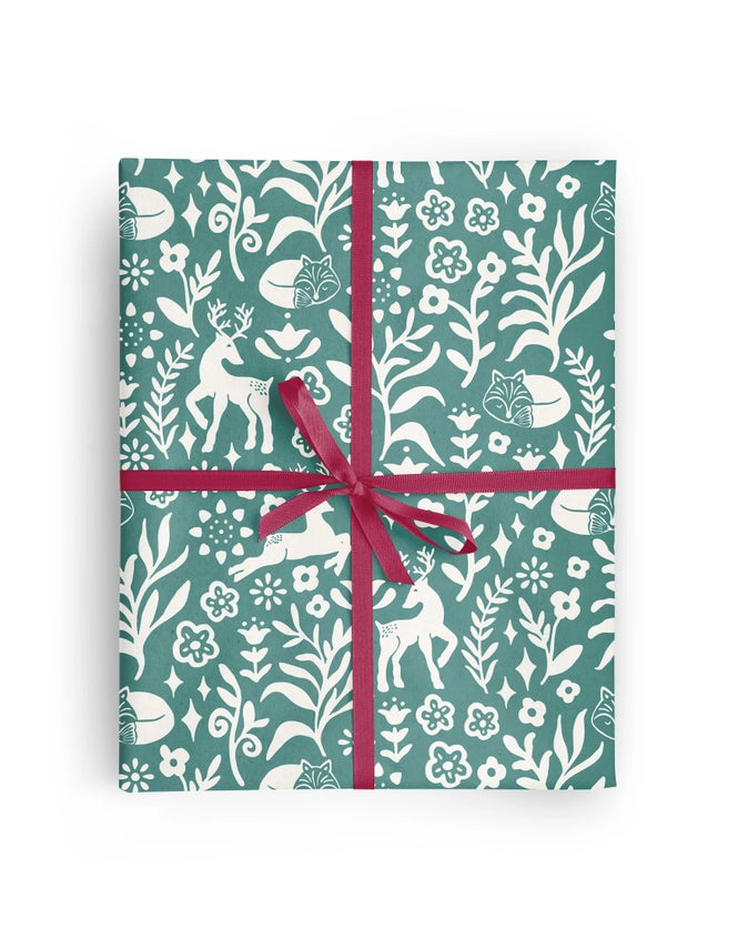 A rectangular gift box wrapped in teal and white botanical patterned paper with white deer motifs, tied with a magenta ribbon in a cross-hatch style and bow, shown on a plain white background.