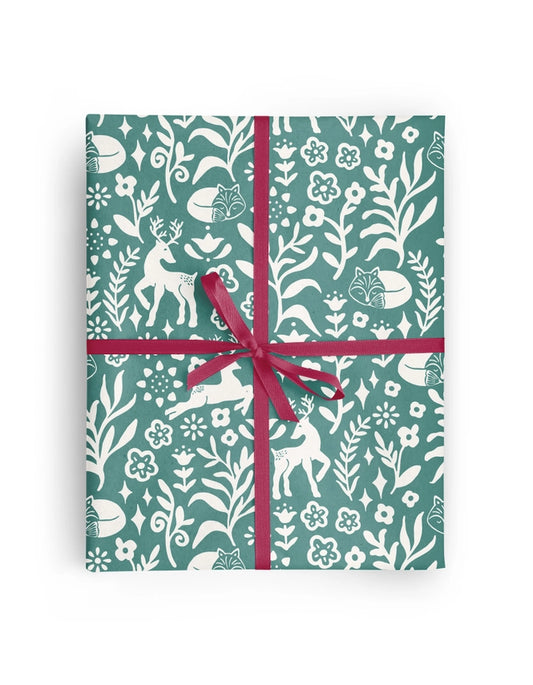 A rectangular gift box wrapped in teal and white botanical patterned paper with white deer motifs, tied with a magenta ribbon in a cross-hatch style and bow, shown on a plain white background.